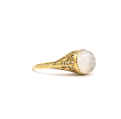 Profile from the opposite side, off the hand, the carved moonstone's nose and chin standing out in silhouette against the bezel edge, with the openwork gallery narrowing sharply into the shank.