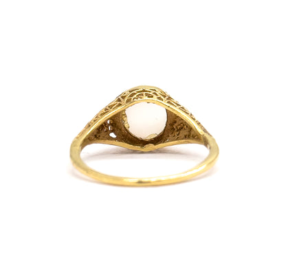 Rear view tipped forward against white, the arched filigree shoulders framing an open-backed bezel so the pale underside of the moonstone shows through the gallery.