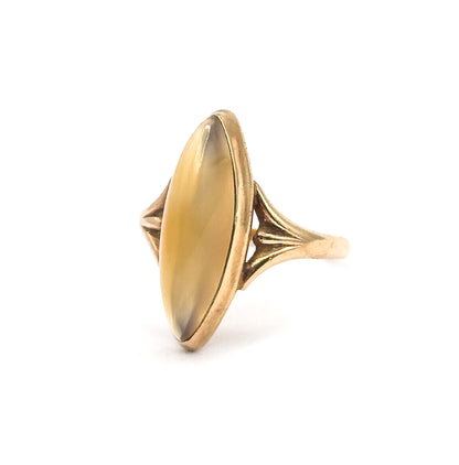 Three-quarter front view against white with the full elongated navette face of the golden brown cabochon on show, the ribbed fan shoulder and slim shank angling back to the right.