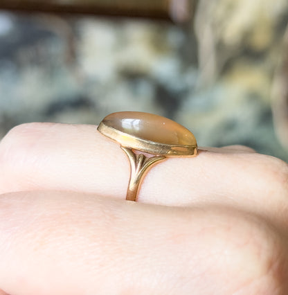 Art Nouveau chalcedony cabochon ring in 10K rose gold, shown on a finger in side view, the elongated marquise stone raised in a smooth bezel above a slender tapering shank.