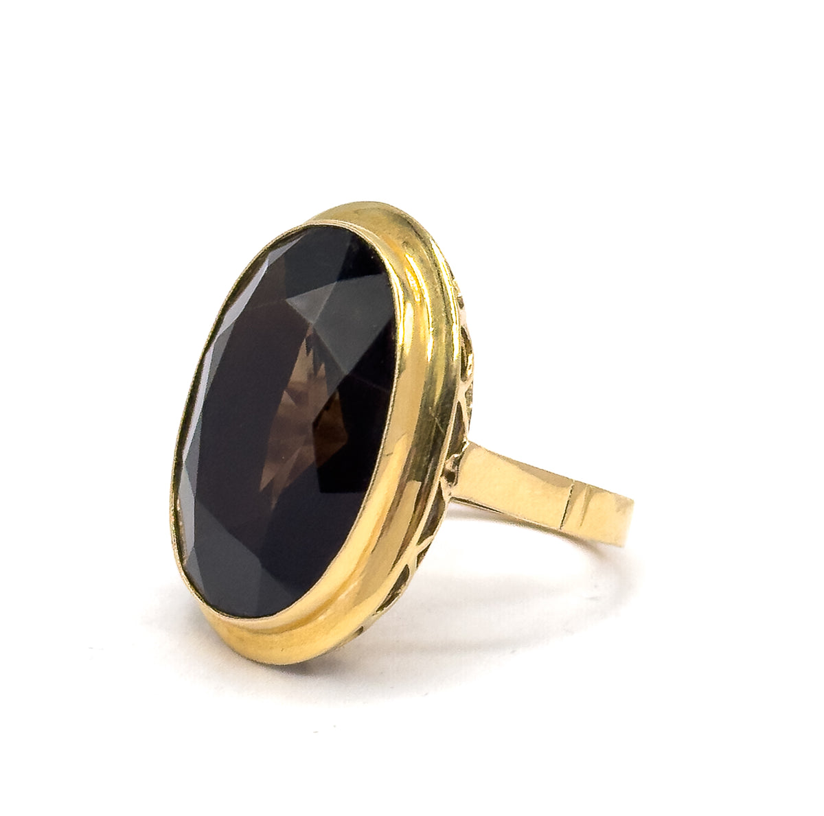 Turned three-quarters so the oval face angles left, the faceted smoky quartz catches light across its broad crown while the yellow gold shank extends to the right.
