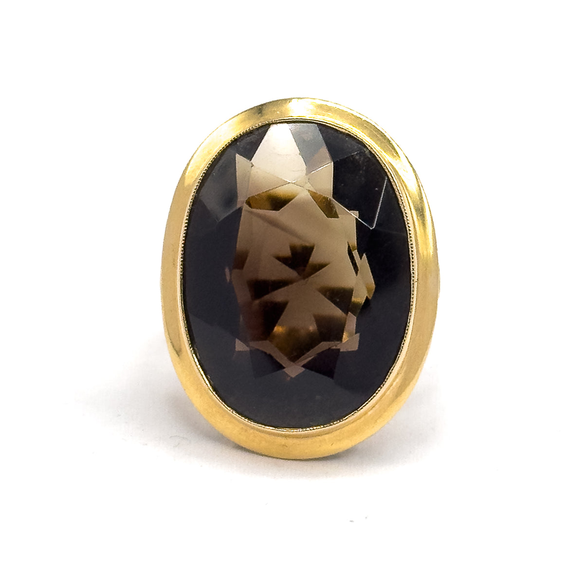 Face-on and filling the frame, the oval smoky quartz sits deep in its smooth yellow gold bezel, its faceted crown paling to honey at the centre against the dark brown depths.
