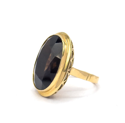 Standing alone on a plain white background at a low side angle, the faceted oval smoky quartz tilted toward the viewer, with the scalloped openwork gallery and flat shank in clear profile.