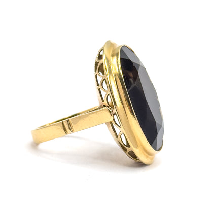 Seen edge-on from the side, the yellow gold bezel rim stands tall around the dark stone while the row of scalloped openwork arcs and the flat, tapering shank read clearly in silhouette.