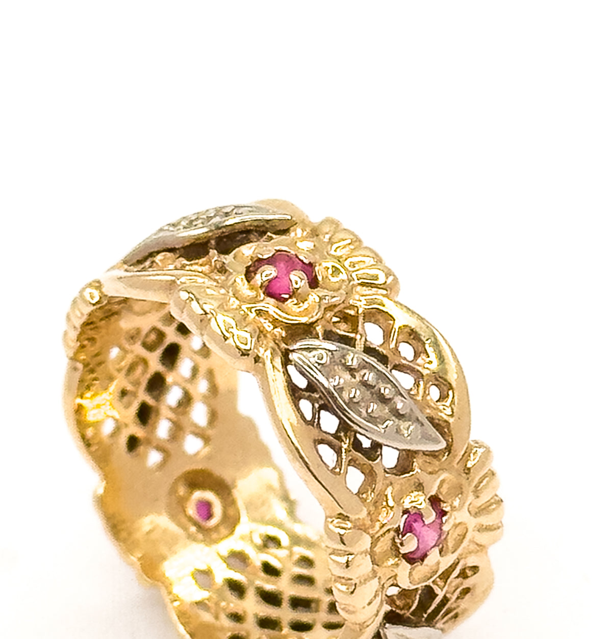 Macro view of a short run of the band, enlarging two deep pinkish red stones in their prongs and a pointed leaf panel of paler metal set over the pierced lattice beneath.