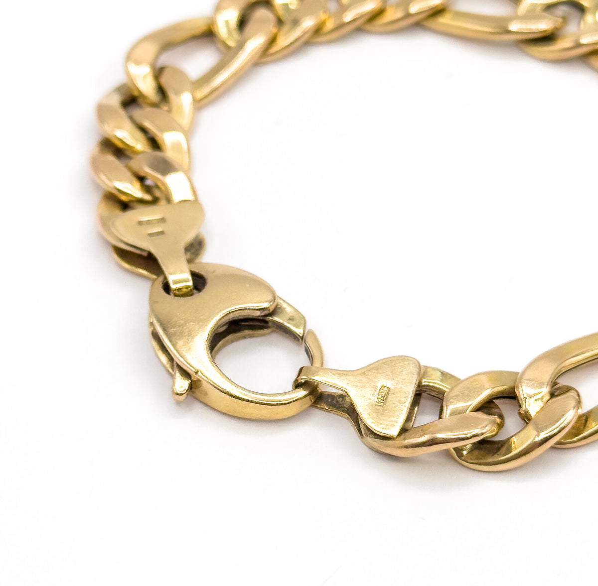 A steep raking view down onto the closed clasp, its rounded body and thumb-piece seen from the side, with tiny stamps visible on the flat tapered end links either side.