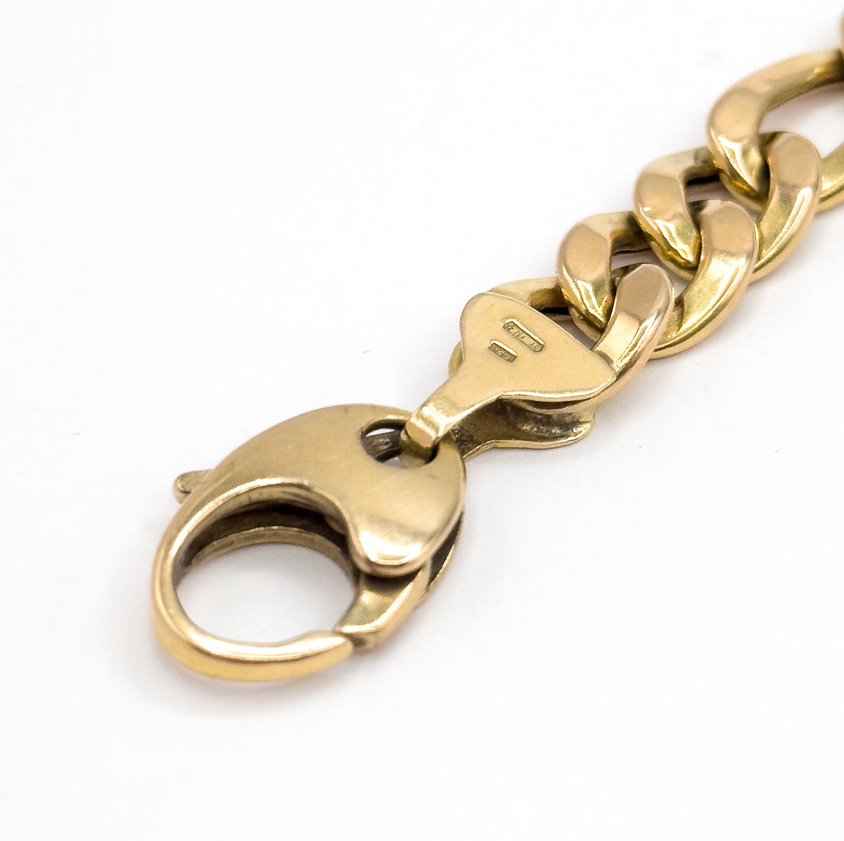 The clasp lying on its back on a white ground, its flat underside and open loop facing the camera, the tapered end link and Figaro chain angling away to the upper right.