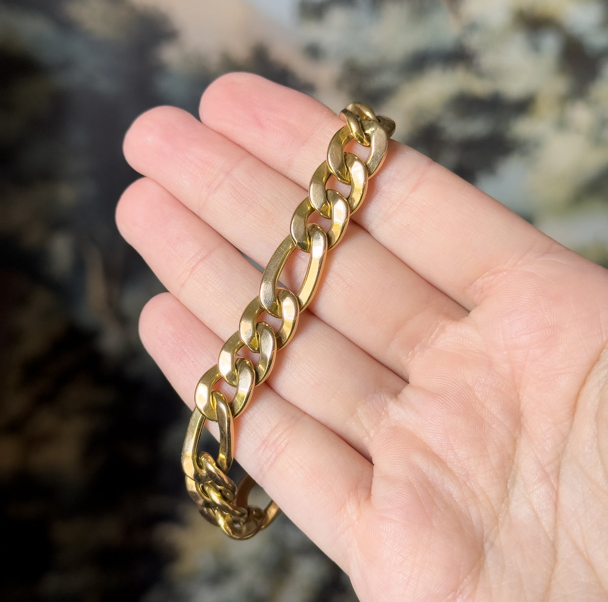 A 14K yellow gold Figaro link bracelet draped across the open fingers of a hand, its polished alternating long and short links catching the light.