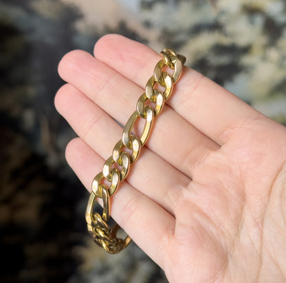 A 14K yellow gold Figaro link bracelet draped across the open fingers of a hand, its polished alternating long and short links catching the light.