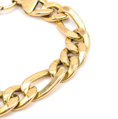 A close crop of the chain curving in a broad U across the frame, where the Figaro rhythm reads clearly: three short yellow gold links followed by one long one, repeating around the bend.
