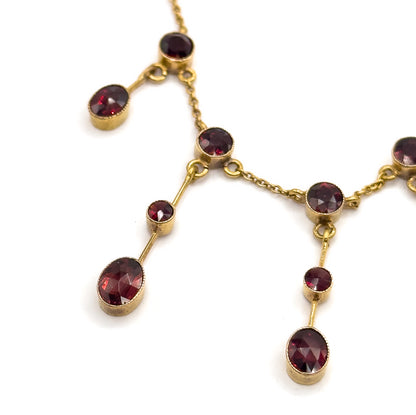 Steeply angled close crop across four fringe drops, the cable chain links running bezel to bezel and the garnets shifting from bright cherry red to a darker brownish red across the row.