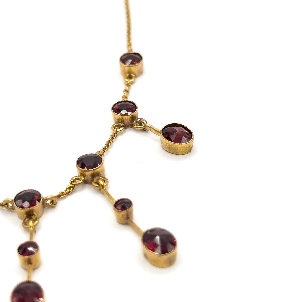 Close view of the upper chain where it enters a bezel station and branches, one garnet swinging out to the side on a short link while the chain continues down to the next bezels below.