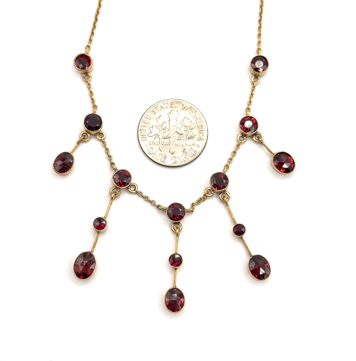 A dime laid between the fringe drops gives the scale, the coin standing roughly as tall as the largest oval garnet beside it, with the bezel-set stones and milgrain frames spread around it.