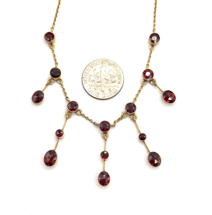 A dime laid between the fringe drops gives the scale, the coin standing roughly as tall as the largest oval garnet beside it, with the bezel-set stones and milgrain frames spread around it.