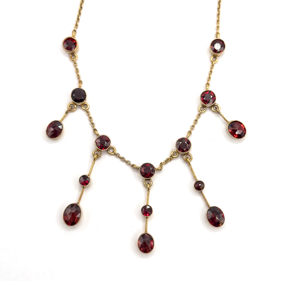 The whole festoon laid flat and symmetrical, showing all fifteen bezel-set garnets at once, the fringe drops hanging in graduated pairs from the chain toward a central drop.