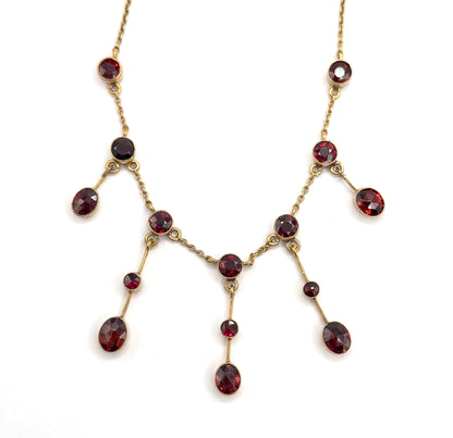 The whole festoon laid flat and symmetrical, showing all fifteen bezel-set garnets at once, the fringe drops hanging in graduated pairs from the chain toward a central drop.