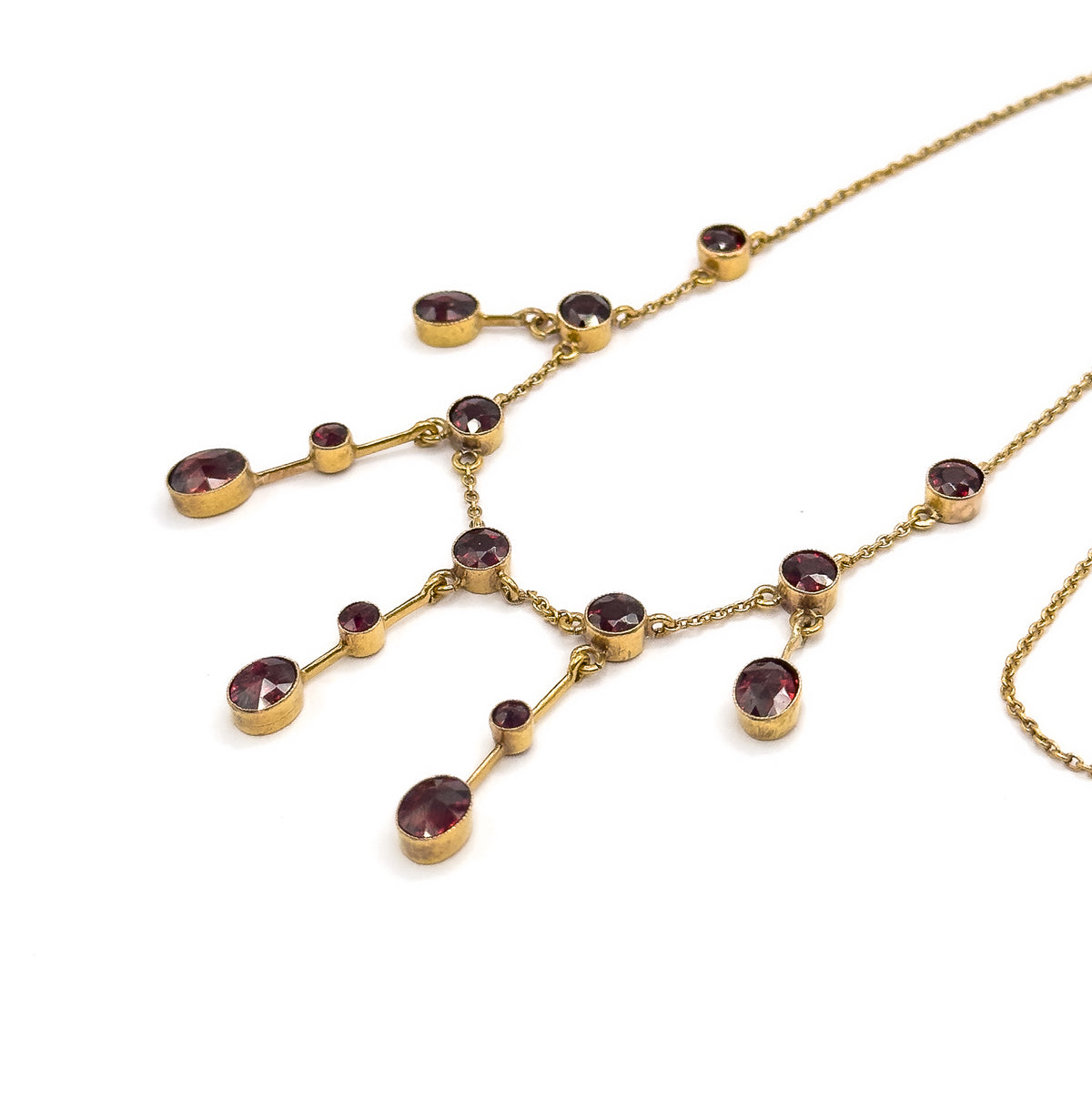 Diagonal view of the festoon centre, the branching gold bars fanning out with a small bezel-set garnet midway along each and a larger oval or round garnet at every tip.