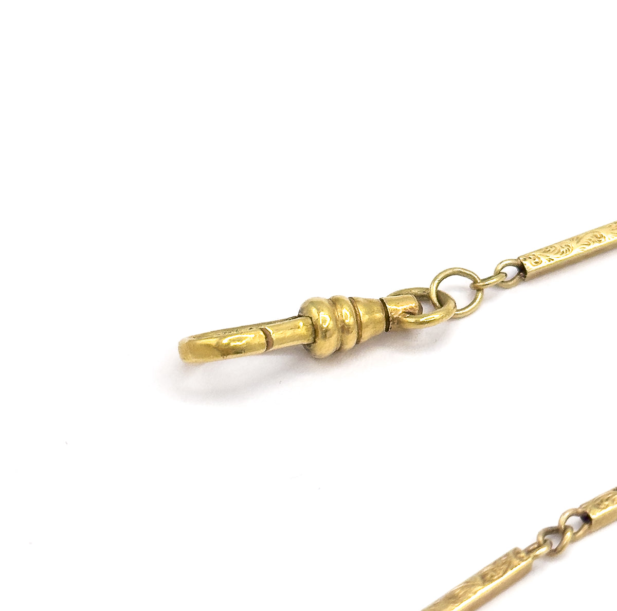 Close-up of the dog clip at one end, its tapered bar and ridged collar linked by a round jump ring to the first engraved bar, with another length of chain at the lower right.