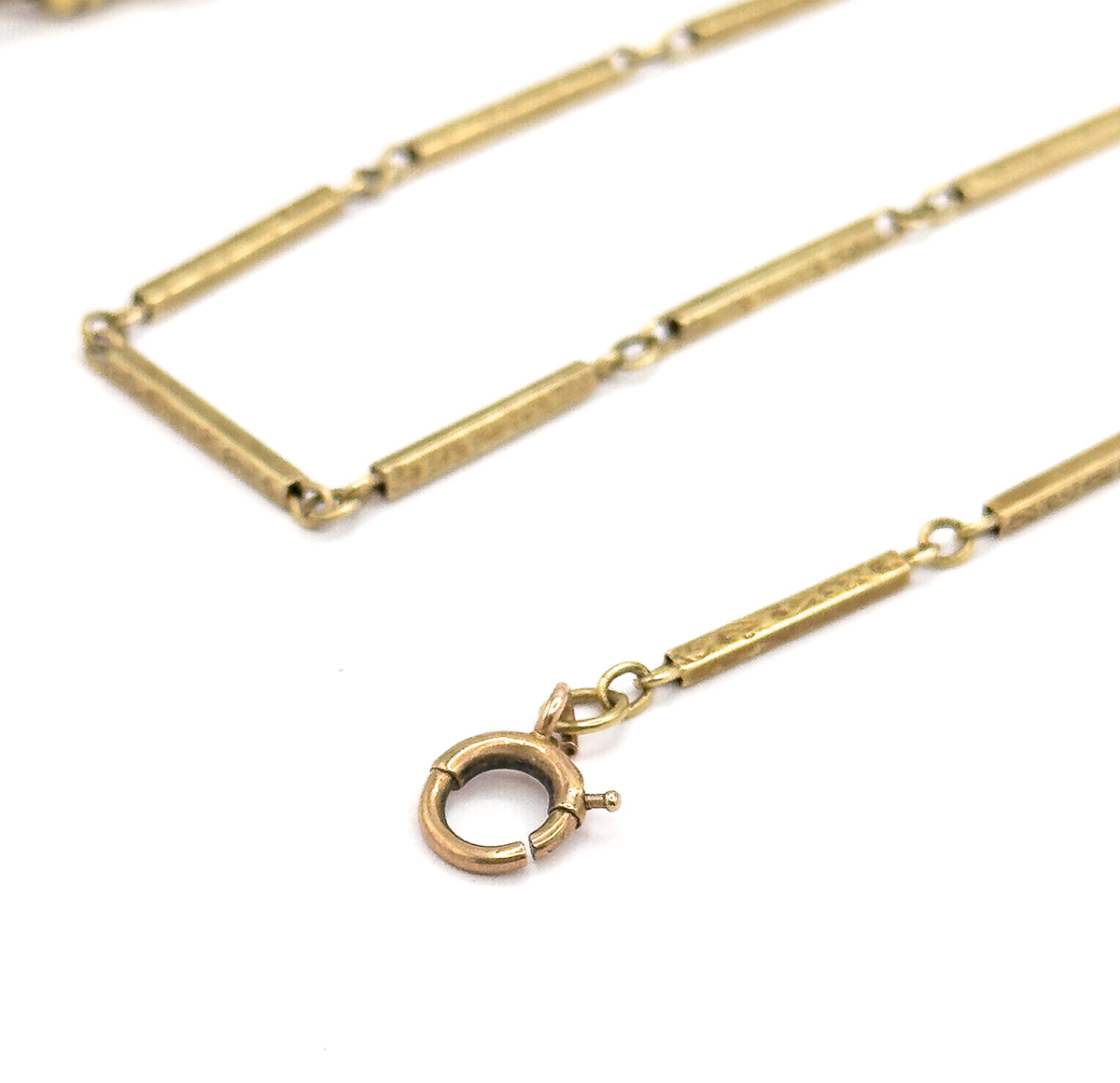 The round spring ring clasp at the opposite end, its small thumb-piece projecting from the side, hanging from a jump ring below the last engraved bar while the chain folds away behind.