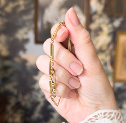 Shown draped over curled fingers so the chain falls in a vertical line, bringing the dog clip and its ribbed swivel collar to the centre between the bar links.