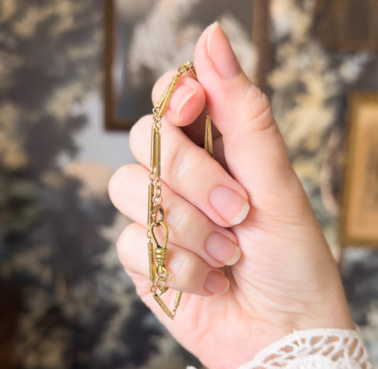 Shown draped over curled fingers so the chain falls in a vertical line, bringing the dog clip and its ribbed swivel collar to the centre between the bar links.