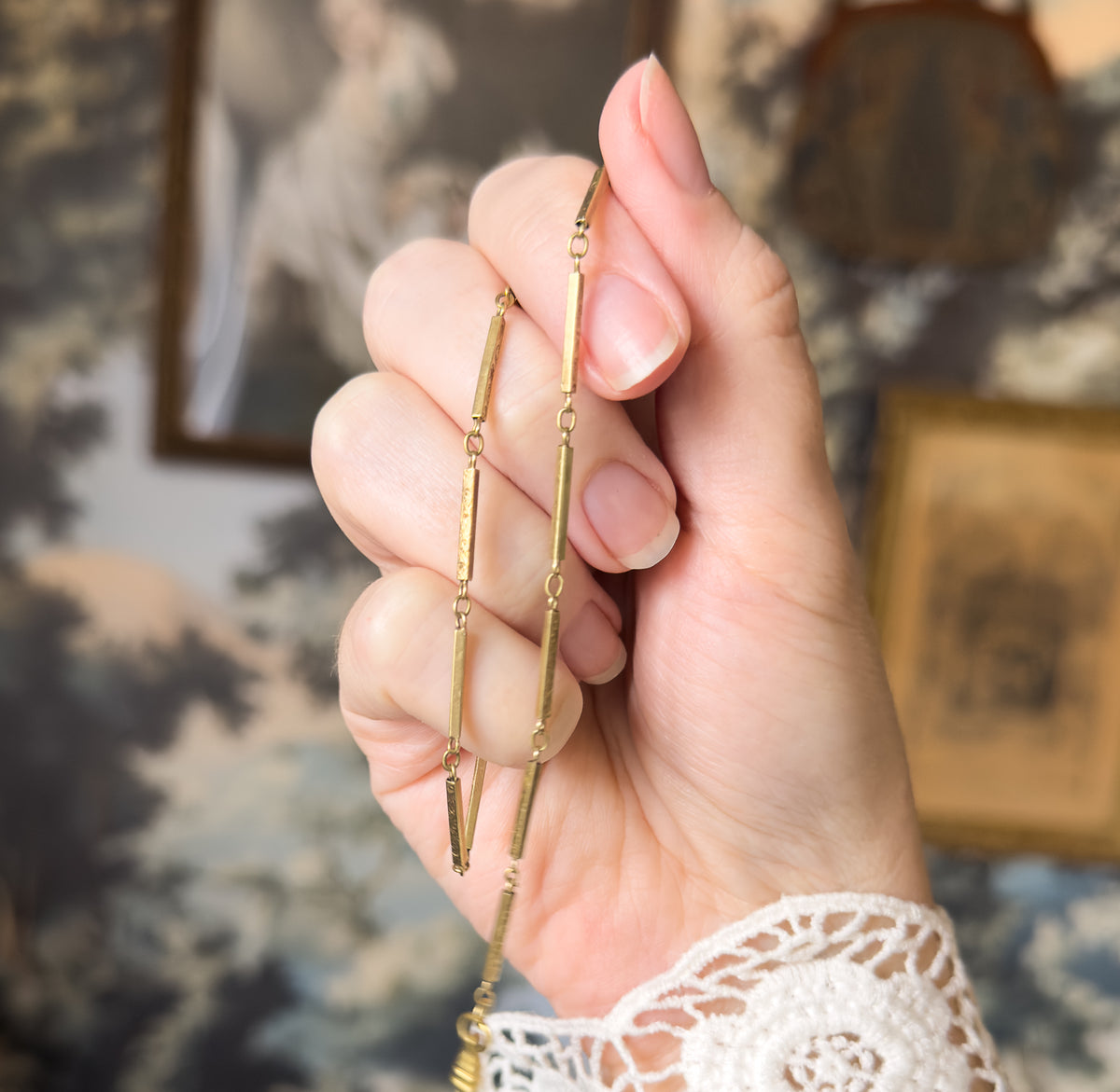 The chain draped over the back of the fingers, a doubled run of narrow bar links joined by small round jump rings descending past the knuckles toward the wrist.