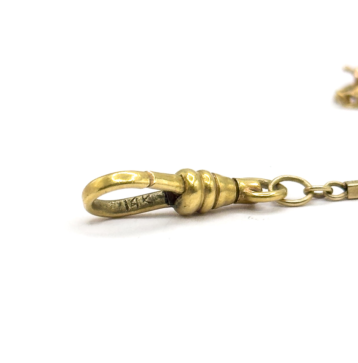Close macro against white of the dog clip alone, its hooked loop carrying a small stamped mark and its ribbed collar meeting a round jump ring that leads off to the bar links.