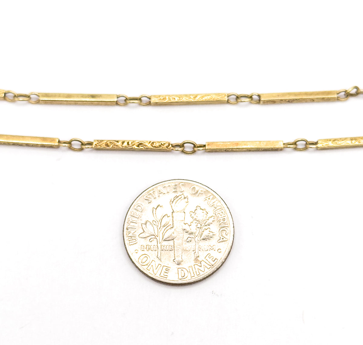 Two parallel runs of the bar link chain laid flat on white beside a dime, the coin showing how narrow each scrolled bar and connecting jump ring really is.