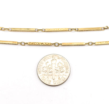 Two parallel runs of the bar link chain laid flat on white beside a dime, the coin showing how narrow each scrolled bar and connecting jump ring really is.