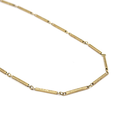 Laid out flat on white in a wide open angle, a long unbroken run of the chain showing the engraved scrollwork on each bar and the tiny jump rings between them.