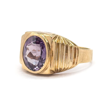 Three-quarter side view showing the oval sapphire face-on in its smooth bezel, pale violet-pink here, with the fluted shoulder sweeping back to the wide yellow gold shank.