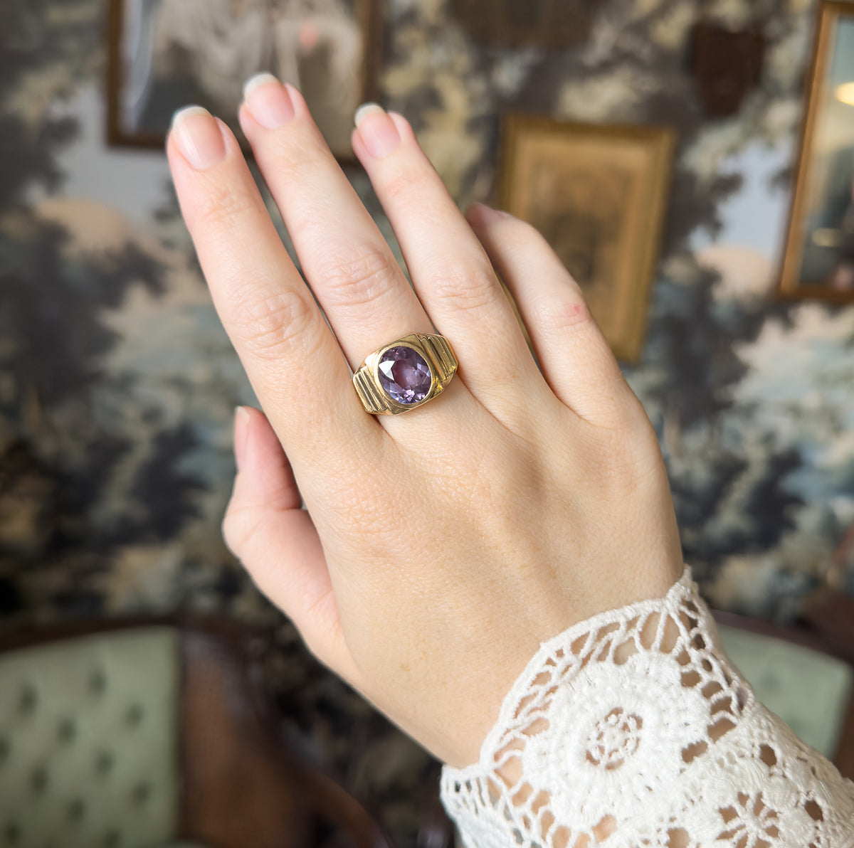 Shown on the middle finger of a raised hand against a patterned backdrop, the ring's scale clear beside the knuckles, with the bezel face angled toward the viewer.