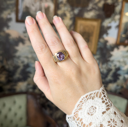 Shown on the middle finger of a raised hand against a patterned backdrop, the ring's scale clear beside the knuckles, with the bezel face angled toward the viewer.