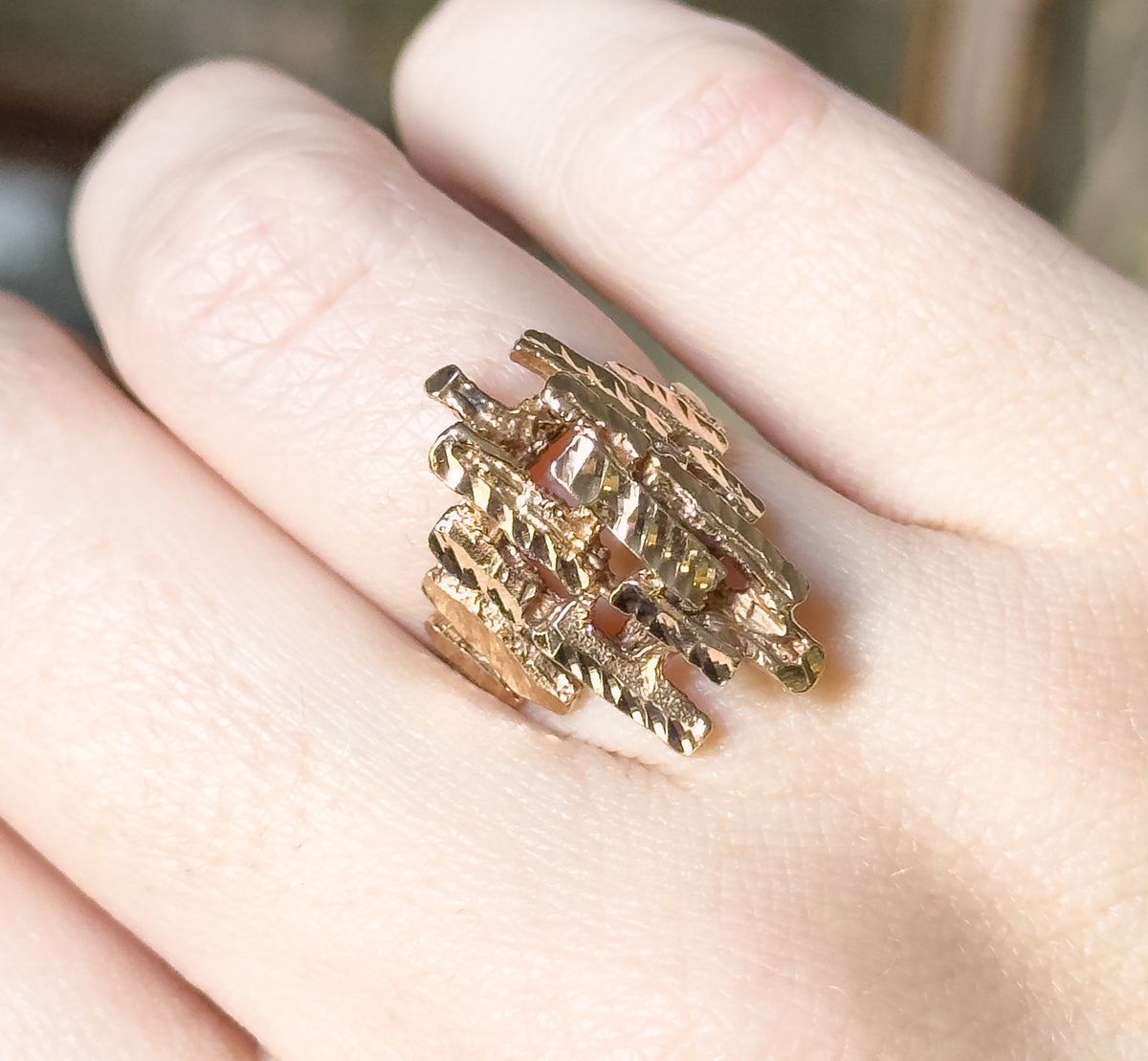 Shown on the hand from a higher angle, the lattice of faceted yellow gold bars reads as a woven block across the finger, its depth and layered stacking clearly visible.