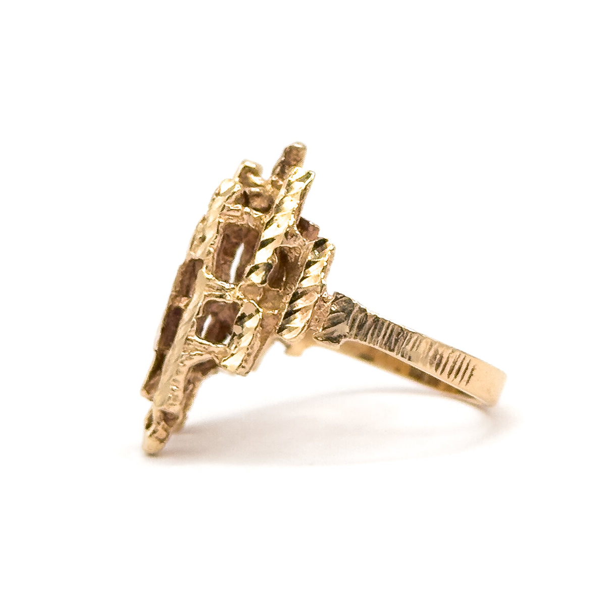 Side profile showing how high the faceted yellow gold head stands above the finger, its bars projecting outward while the shank narrows and sweeps away to the right.