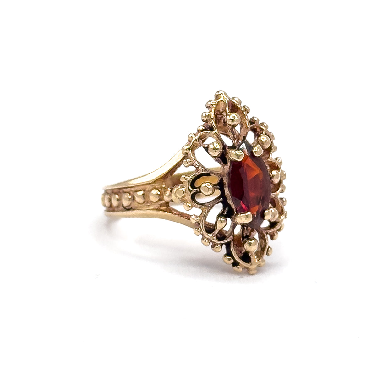 Off the hand against white, a three-quarter side view showing the beaded split shoulders rising to the raised navette face and the marquise garnet seen edge-on in its bezel.