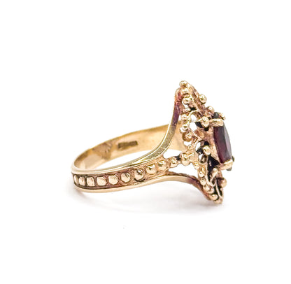 A direct side profile against white, the inside of the band showing faint stamped marks, with the row of beads along the shank leading up to the garnet seen edge-on in its prongs.