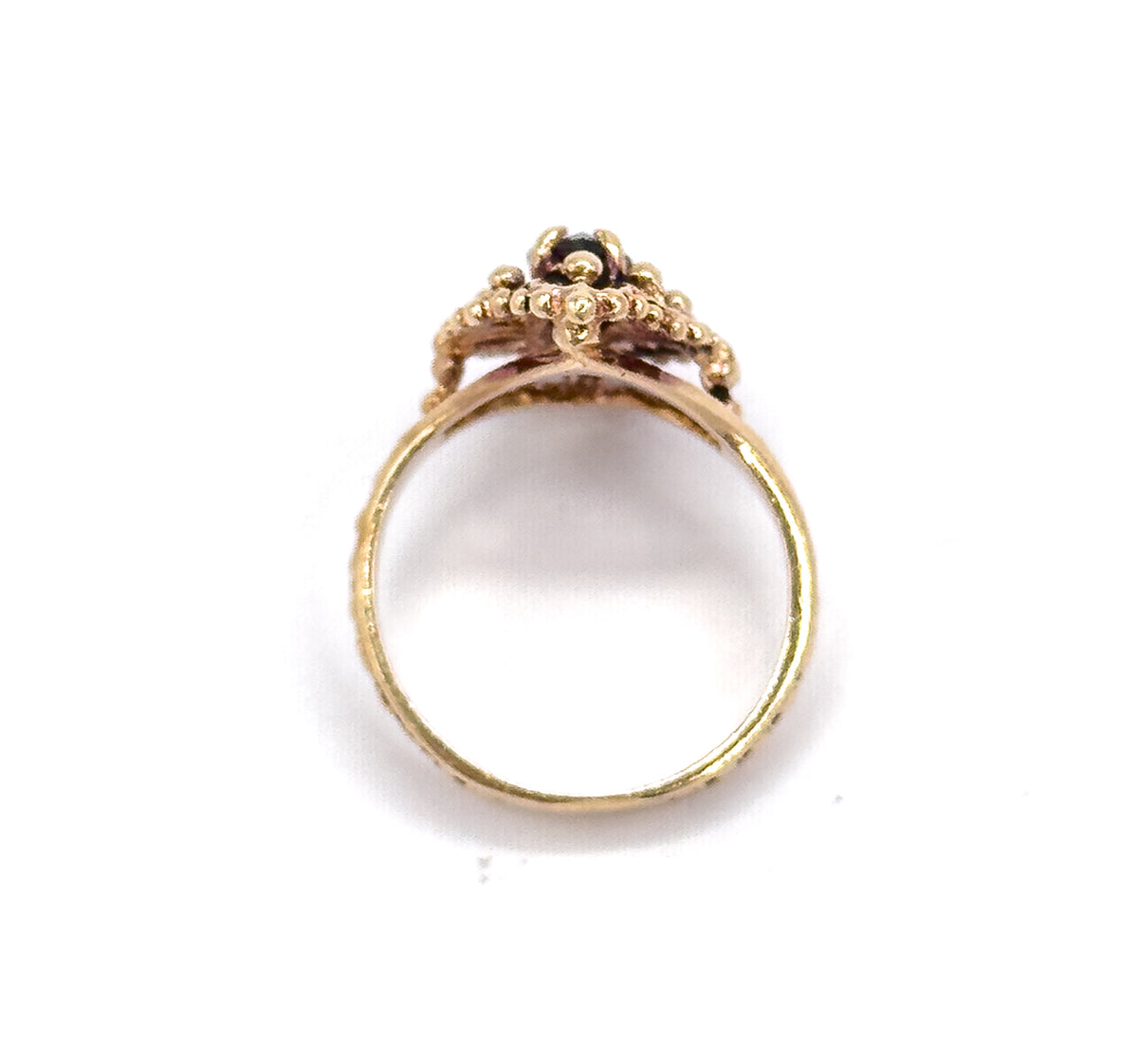 Standing upright against white, the full circle of the slim shank is seen head-on, with the beaded navette face above showing the dark marquise garnet peeking between its bead clusters.