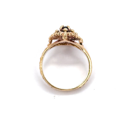 Standing upright against white, the full circle of the slim shank is seen head-on, with the beaded navette face above showing the dark marquise garnet peeking between its bead clusters.