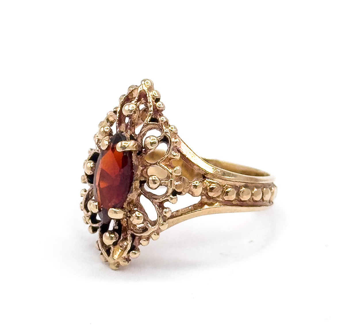 A three-quarter view with the navette face turned to the left, showing the marquise garnet in its bead-edged bezel raised high above the split shoulders that flare out from the beaded shank.