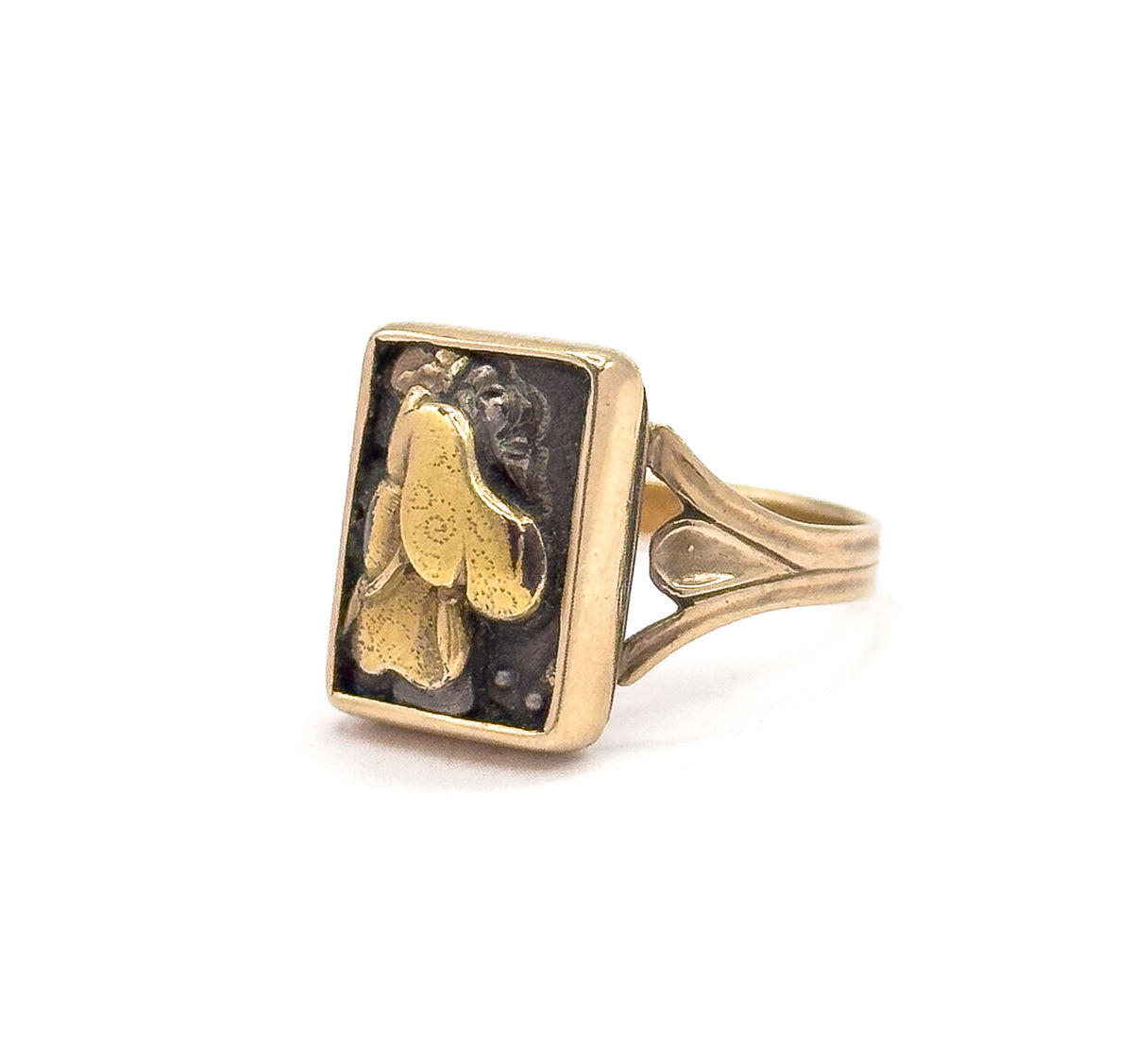 Three-quarter front view on white, the dark textured Shakudo panel's raised figural design filling the rectangular yellow gold bezel, with the teardrop-pierced shoulder and shank angled behind.