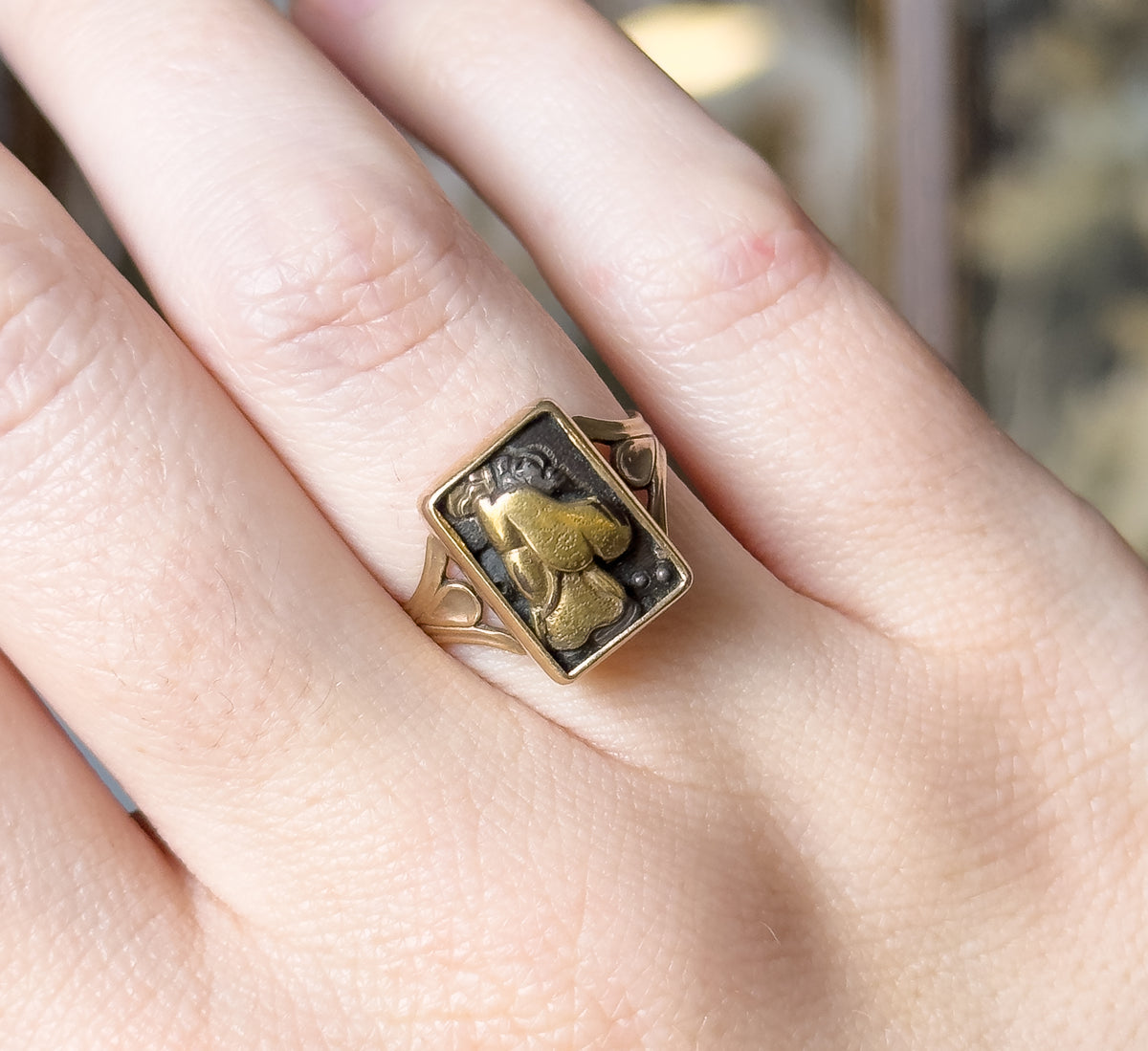 Straight-down view, shown on a finger with the hand filling the frame, so the small rectangular panel reads clearly against the knuckle, its pierced shoulders curving away on each side.