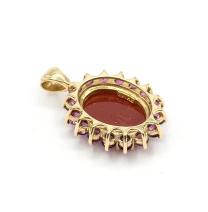 The reverse of the pendant, showing the open back of the cameo setting, the yellow gold gallery with its prongs gripping each garnet, and the hinged bail at the top.