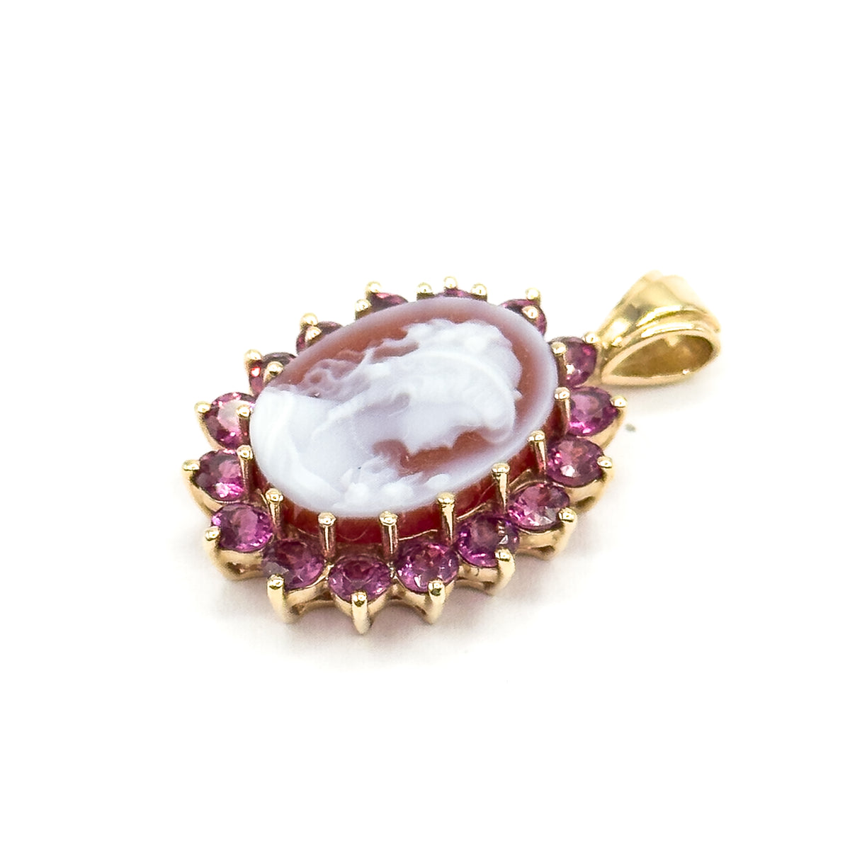 Angled three-quarter view against white, the carved cameo face tilted to show the depth of the yellow gold frame, the ring of pinkish-purple garnets in their prongs, and the bail at the side.