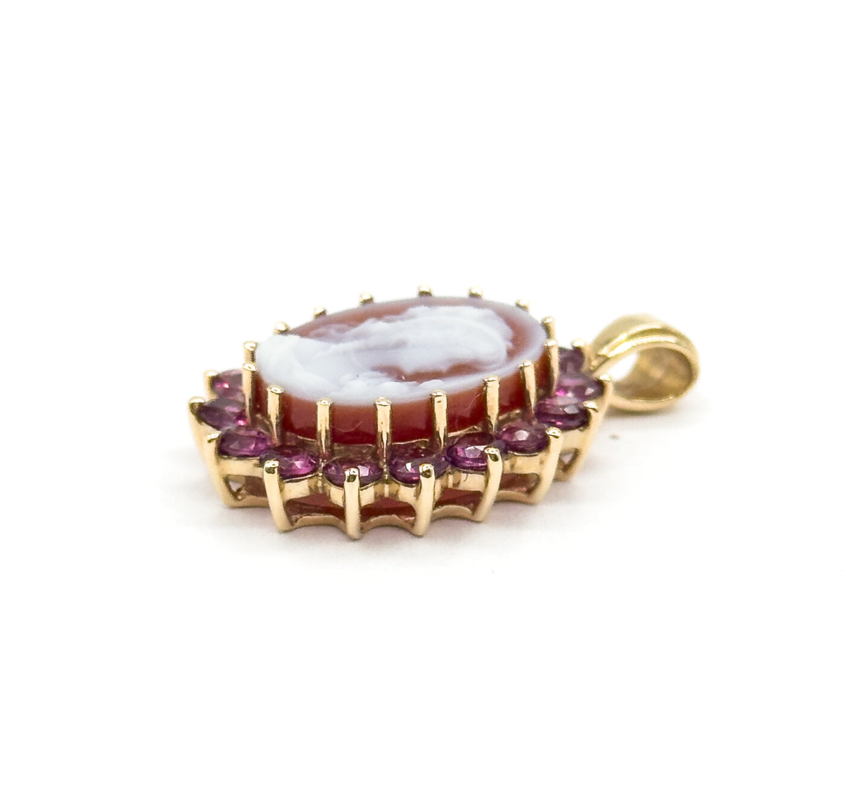 A low side view against white, the cameo almost edge-on so the tall gold gallery prongs beneath the garnet halo and the curve of the bail stand out in profile.