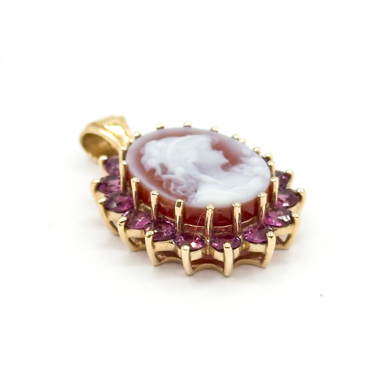 Tilted so the carved profile at the centre of the cameo reads clearly, with the garnet halo sweeping around the lower edge and the bail angled away behind the gold frame.