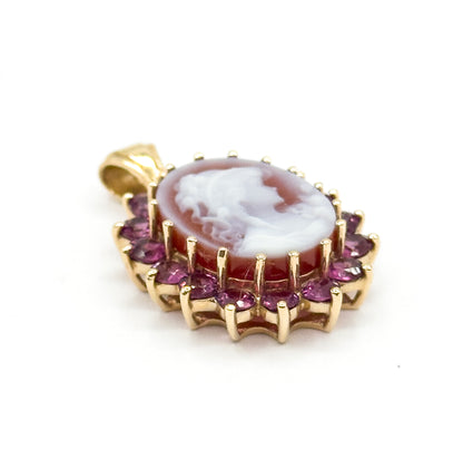 Tilted so the carved profile at the centre of the cameo reads clearly, with the garnet halo sweeping around the lower edge and the bail angled away behind the gold frame.
