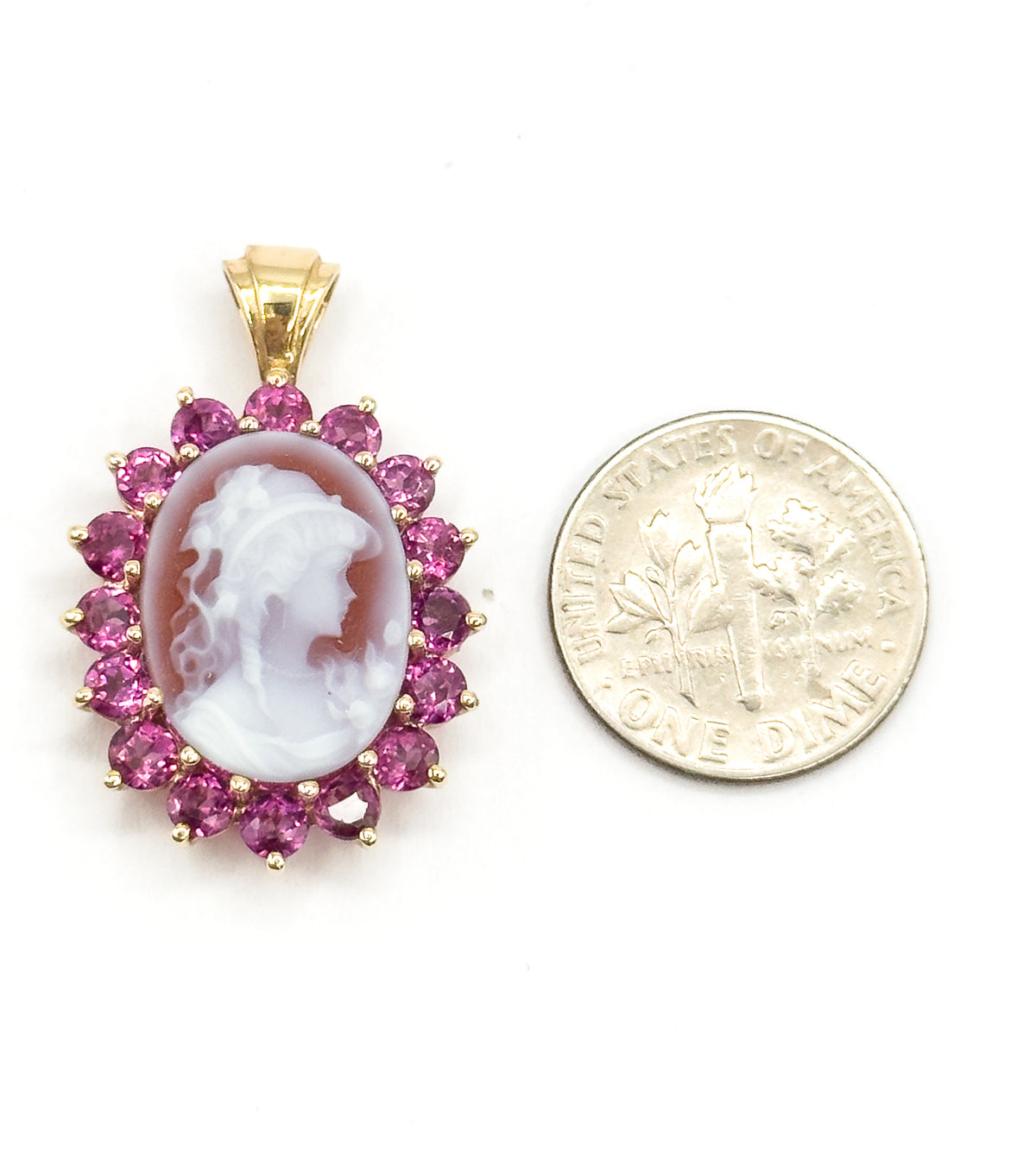 Shown flat beside a dime for scale, the pendant only a little taller than the coin, its ribbed yellow gold bail upright above the garnet halo and carved cameo.