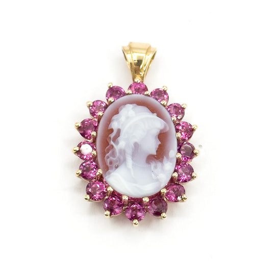 Straight-on front view against white, the carved profile facing right and every one of the sixteen prong-set garnets visible in a full ring, with the ribbed bail centred above.