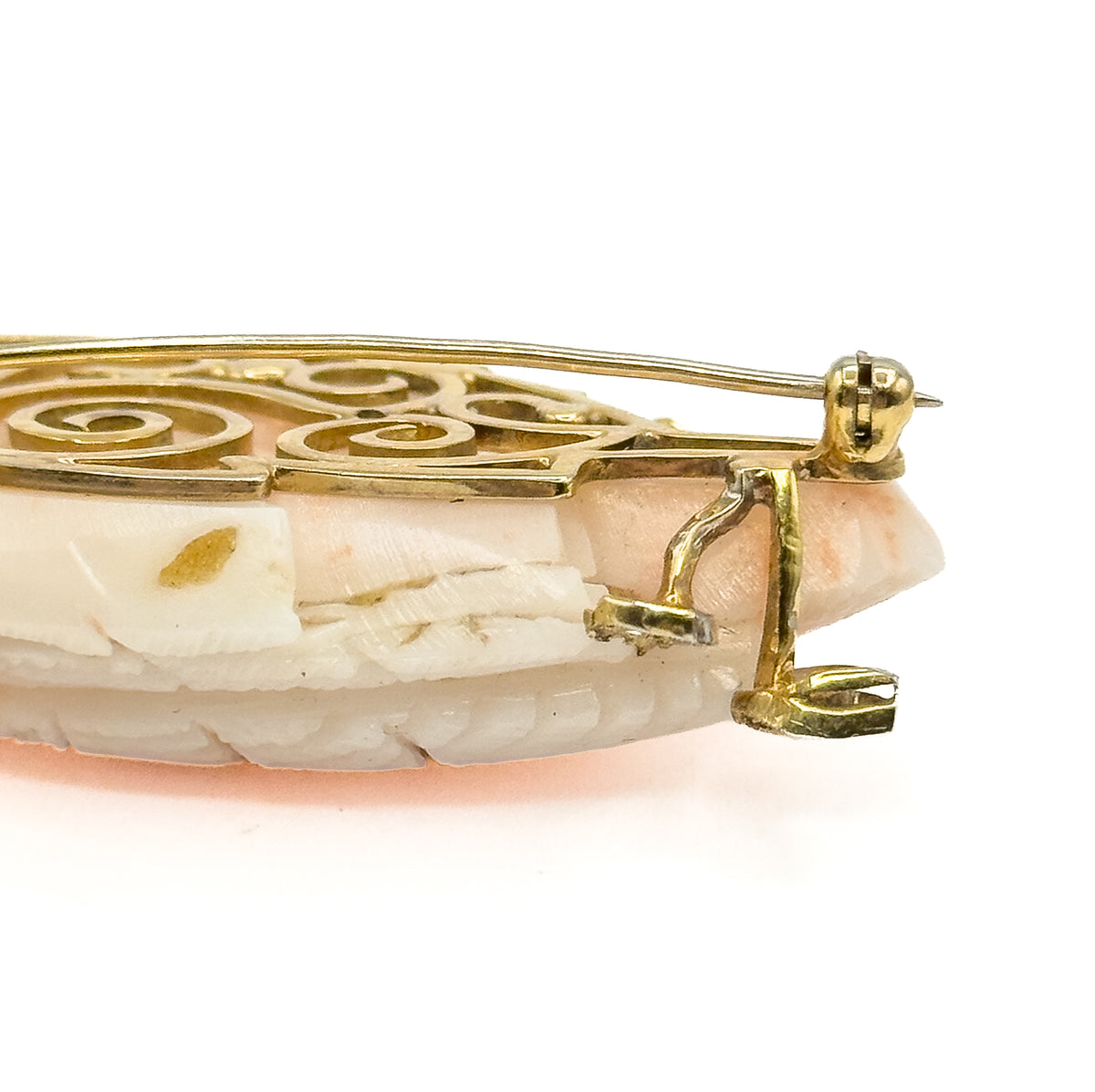 Seen edge-on from behind, showing the scrolled openwork gallery, the long pin stem running through its hinge, and the gold catch below the carved coral's profile.